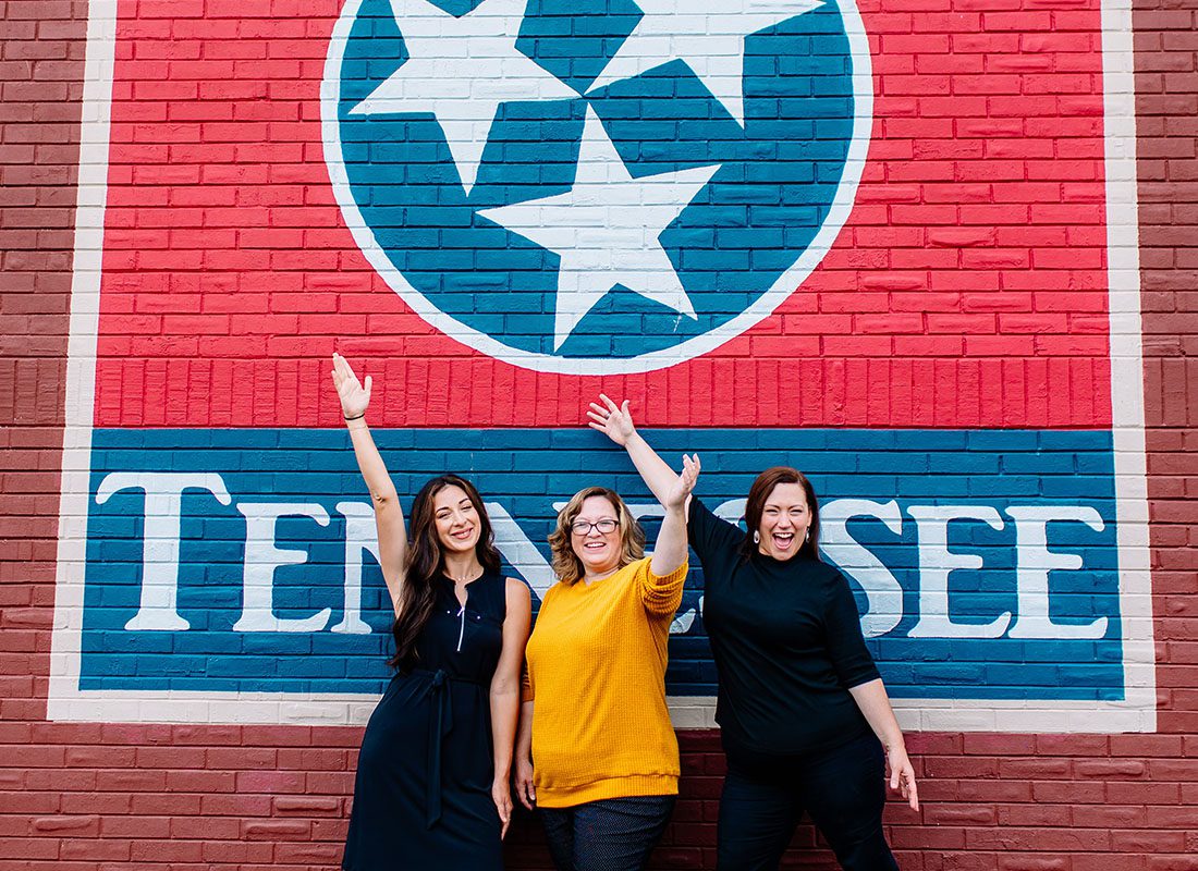 Mt. Juliet, TN - Guess Insurance Agency LLC Team Standing in Front of a Brick Building With Tennessee Art on it